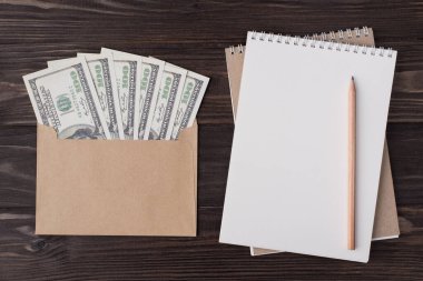 Tepedeki düz görünümde, içi dolar dolu el sanatları zarfının resmi yer almaktadır. Boş defter kalemi, ahşap arka planda, kopyalama alanı ile izole edilmiştir.