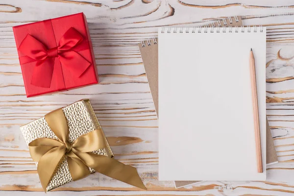 Noel tatili konsepti. Tepedeki düz görünümde boş bir defter kalemi ve küçük hediyelerin fotosu var. Hafif ahşap arka planda, kopyalanmış.