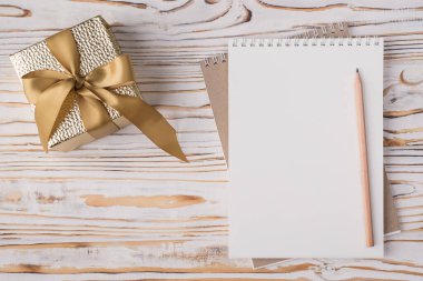 Tepedeki düz görünümde boş bir defter kalemi ve hafif ahşap zemin üzerinde izole edilmiş altın hediye kutusunun fotosu yer almaktadır.