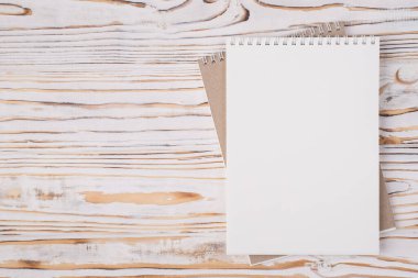 Tepedeki düz görünümde, sağ tarafa yerleştirilmiş boş bir defterin fotosu var. Kopyalama alanı ile izole edilmiş, hafif ahşap zemin üzerinde.