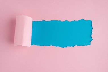 Tepede mavi arkaplanlı yırtık pembe kağıdın fotosu var.