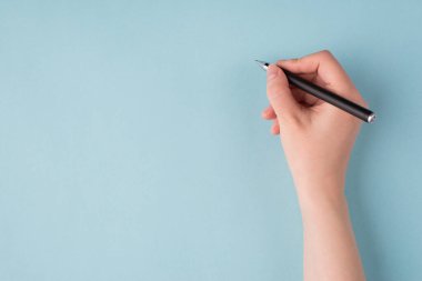 Top above overhead close up first person view photo of girl's right hand holding black pen starting to write isolated over blue color pastel background clipart