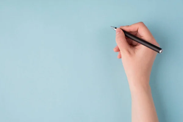 Top above overhead close up first person view photo of girl's right hand holding black pen starting to write isolated over blue color pastel background