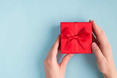 Doğum günü konseptindeki en iyi hediye. Yukarıdaki tepede yakın plan. Kadın eli fotoğrafında Pastel renkli arka planda izole edilmiş küçük canlı bir kutu gönderiliyor.