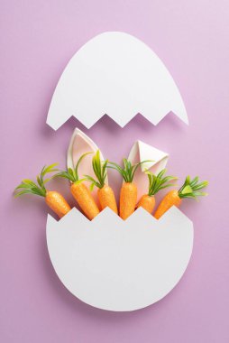 Şık Paskalya temamızı keşfet. Havuç ve tavşan kulaklarının pastel bir leylak yüzeyde yumurta kabuğundan fırlayan dikey fotoğrafı, selamlama ya da promosyon içeriği için tasarlandı
