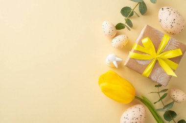 Paskalya sofrası kurma fikri çok hoş. Kahverengi el işi kağıtları, sarı lale, okaliptüs, tavşan heykeli, benekli bıldırcın yumurtaları, açık bej arka planda serili, kopya için boşluk.