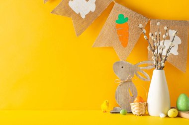 Bahar Paskalya düzenlemesi, dekoratif eşyalar, çok renkli yumurtalar, söğüt ağacı dolu bir vazo ve eski moda çelenk ile dolu yan manzara masası turuncu duvar arka planında, mesajlaşma için yer