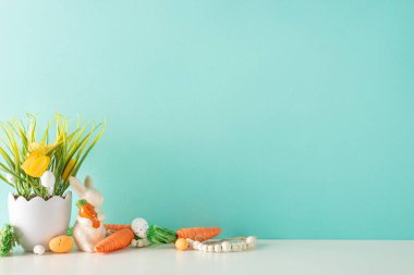 Bahar Paskalya düzenlemesi, dekoratif eşyalarla dolu masada yan görünüm sunumu, havuçlu tavşan, parlak yumurta, boncuklar, açık mavi duvarlı bitki temalı vazo, mesajlaşma için alan