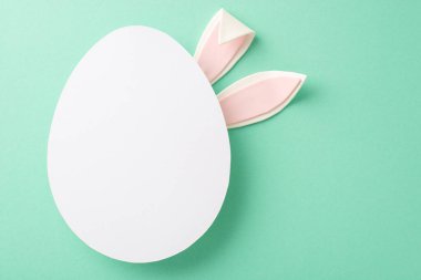 Paskalya yaratıcılığı vizyonu: Turkuaz bir arka planda tavşan kulağı getirmenin üst görünümü, metin veya onaylar için yumurta şeklinde bir alan