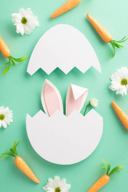 Paskalya kaprisli sahnesi. Yumurta kabuğu kırığından bakan sevimli tavşan kulaklarının dikey görüntüsü, Paskalya Tavşanı 'nın havuç atıştırmalıkları, ve turkuaz bir alanda papatya çayı, mesaj veya reklam için bir alan.