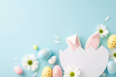 Garip Paskalya hayal gücü konsepti. Mavi yüzeyinde papatya ve çok renkli yumurtalarla bölünmüş yumurtalardan görülebilen şirin tavşan kulaklarının üst görüntüsü özel mesajlar veya reklamlar için alan sağlıyor.