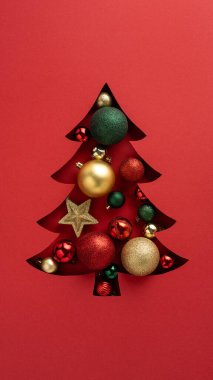 Kırmızı bir Noel ağacı kesim tasarımına yerleştirilmiş parlak süslemeleri olan şenlikli dikey bayram kartı.