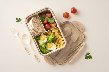 Haşlanmış yumurta, yeşillik, dilimlenmiş domates, makarna ve pirinç keklerinin yer aldığı besleyici bir beslenme çantası, sağlıklı beslenme ve yemek hazırlığı içeriyor. Kullanım için plastik çatal ve kaşık içerir