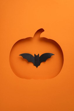 Yaratıcı dikey Cadılar Bayramı kompozisyonu turuncu bir yarasa siluetiyle balkabağı kesimini gösteriyor