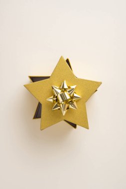 Yıldız şeklinde dikey altın hediye kutusu, dekoratif bir fiyonk, kutlamaları ve şenlikli anları simgeliyor.