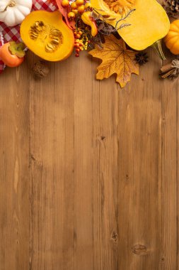 Renkli sonbahar sebzeleri ve Şükran Günü yapraklarıyla çevrili tahta bir masanın dikey görüntüsü.