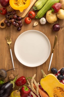 Taze sebzeler ve güz hasadı ürünleriyle çevrili merkezi bir tabağın yer aldığı bir Şükran Günü sofrası kurulumunu gösteren dikey manzara, mevsimsel kutlamaları vurguluyor.