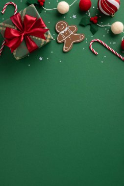 Kırmızı kurdeleli, zencefilli, bastonlu, şeker kamışlı, Noel neşesi ve mevsimsel promosyon için yeşil bir zeminde süslenmiş bir hediye içeren dikey bir Noel sahnesi.