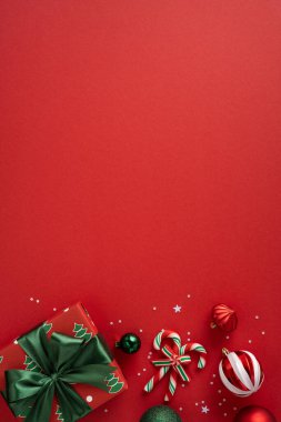 Dikey hareketli bir kırmızı bayram arkaplanında bir paket hediye, şeker kamışları, mücevherler, yıldızlar ve kurdeleler, Noel ve Yeni Yıl kutlamalarının sinyalleri yer alıyor. Parlak renkler neşeyi, sıcaklığı ve şenlik neşesini çağrıştırır.