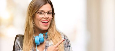 Genç öğrenci kadınla kulaklık ve uzak yan parmak ile işaret sırt çantası