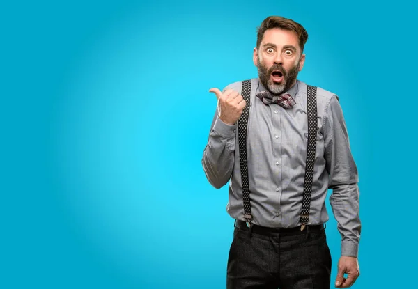 Middle age man, with beard and bow tie happy and surprised cheering expressing wow gesture pointing up