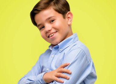 Kendinden emin ve mutlu bir büyük doğal ile çapraz kollu yeşil gözlü yakışıklı yürümeye başlayan çocuk gülümseme sarı arka plan üzerinde gülüyor