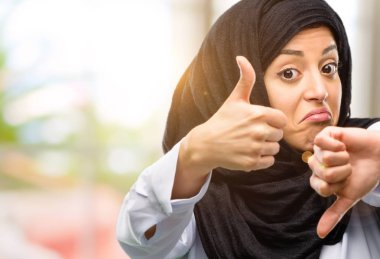 Şüphe ve hayal kırıklığı ifade bir karar almak yukarı ve aşağı, başparmak ile karışık hijab giyen genç Arap kadın çalışıyor