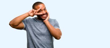 Göz göz kırpıyor ve mavi arka plan üzerinde izole bir öpücük üfleme zafer jest olarak parmak kameradan bakıyorsun sakallı Afrikalı-Amerikalı adam