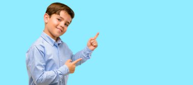 Mavi arka plan üzerinde uzak yan parmak ile işaret yeşil gözlü yakışıklı yürümeye başlayan çocuk