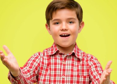 Kendinden emin ve mutlu sarı arka plan üzerinde bir büyük doğal gülümseme hoş geldiniz hareketi ile yeşil gözlü yakışıklı yürümeye başlayan çocuk