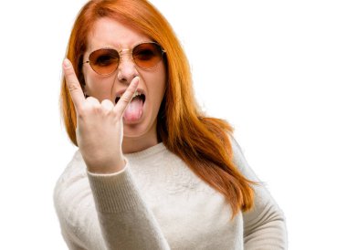 Eller genç güzel kızıl saçlı kadın olan rock simge yapma, bağırarak ve dilini çıkarmış kutluyor beyaz arka plan üzerinde izole