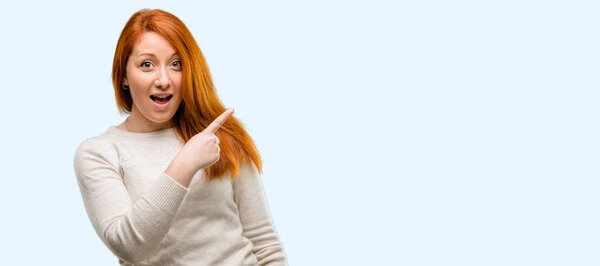 Beautiful young redhead woman pointing away side with finger isolated over blue background