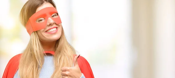 Young super woman smiling broadly showing thumbs up gesture to camera, expression of like and approval