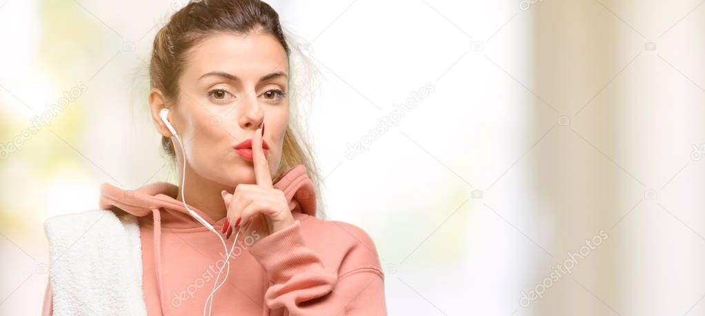 Young sport woman wearing workout sweatshirt with index finger on lips, ask to be quiet. Silence and secret concept