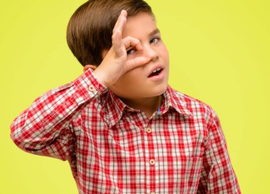 Parmakları Tamam jest olarak kameradan bakıyorsun yeşil gözlü yakışıklı yürümeye başlayan çocuk. Taklit dürbün, güzel gözleri ve gülümseme sarı arka plan üzerinde