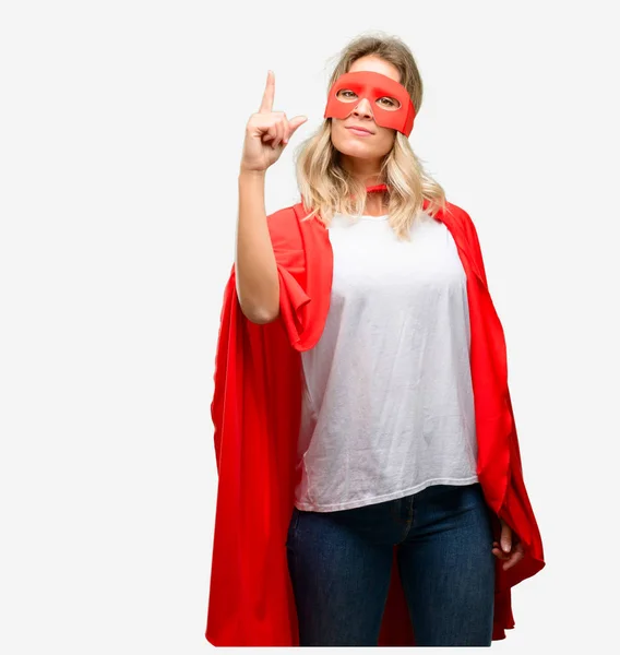 Young super hero woman wearing cape raising finger, the number one