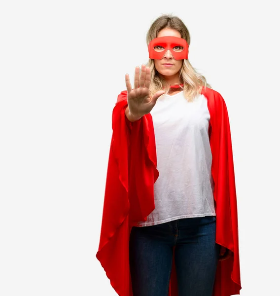Young super hero woman wearing cape annoyed with bad attitude making stop sign with hand, saying no, expressing security, defense or restriction, maybe pushing
