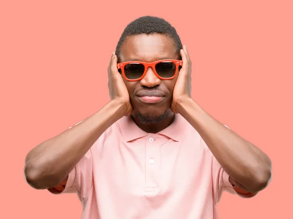 迷惑な騒音を無視しての耳をカバーするサングラスを身に着けているアフリカの黒人男性の聴覚音を避けるために耳をプラグします 騒々しい音楽が問題 — ストック写真