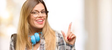 Genç öğrenci kadınla kulaklık ve uzak yan parmak ile işaret sırt çantası