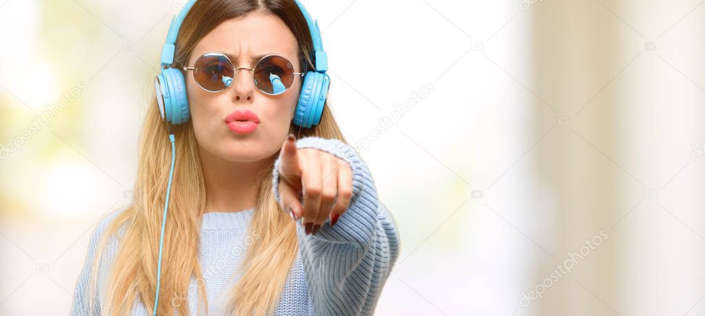 Young woman listen to music with headphone pointing to the front with finger