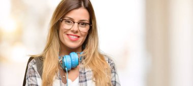 Genç öğrenci kadın kendinden emin ve mutlu bir büyük doğal gülümseme gülmek ile çapraz kollu sırt çantası ve kulaklık ile