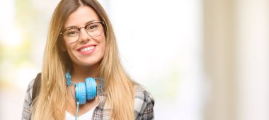 Genç öğrenci kadın sırt çantası elinde boş reklam banner, reklam, teklif veya duyuru, büyük kağıt billboard iyi poster ve kulaklık ile