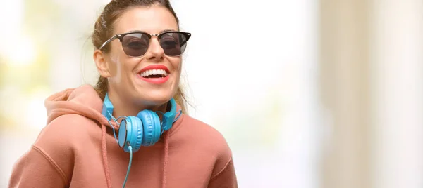 Young sport woman with headphones and sunglasses happy and surprised cheering expressing wow gesture, pointing with finger