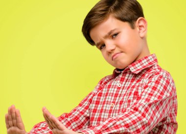 Yeşil gözlü yakışıklı yürümeye başlayan çocuk güvenlik, savunma veya kısıtlama, belki üzerinde sarı arka plana iterek ifade eliyle dur işareti yapma, Hayır, kötü tutum ile rahatsız