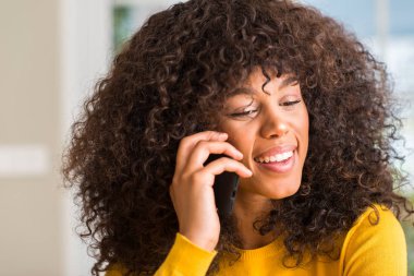 Afrikalı-Amerikalı kadın ayakta ve diş gösterilen kendine güvenen bir gülümsemeyle gülümseyerek mutlu bir yüz ile Smartphone kullanarak