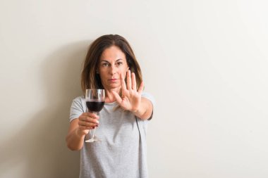 Orta yaş kadın ile bir bardak kırmızı şarap içme dur işareti ile ciddi ve kendine güvenen ifade, savunma hareketi yaparken el açmak