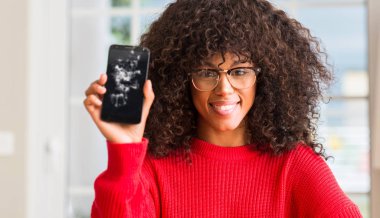 Kırık smartphone ile ayakta ve diş gösterilen kendine güvenen bir gülümsemeyle gülümseyerek mutlu bir yüz tutan Afrikalı-Amerikalı kadın