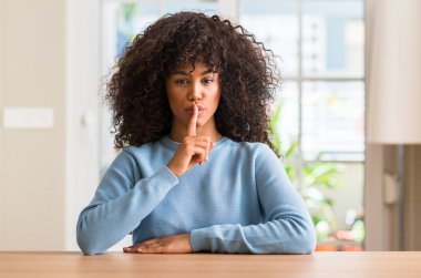 African american woman at home asking to be quiet with finger on lips. Silence and secret concept. clipart