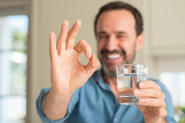 優秀なシンボルの指で サインをしている水のガラスを飲む中年男性 — ストック写真