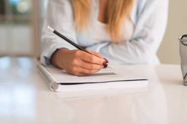 Young beautiful woman hands writting on a book while studying at home clipart
